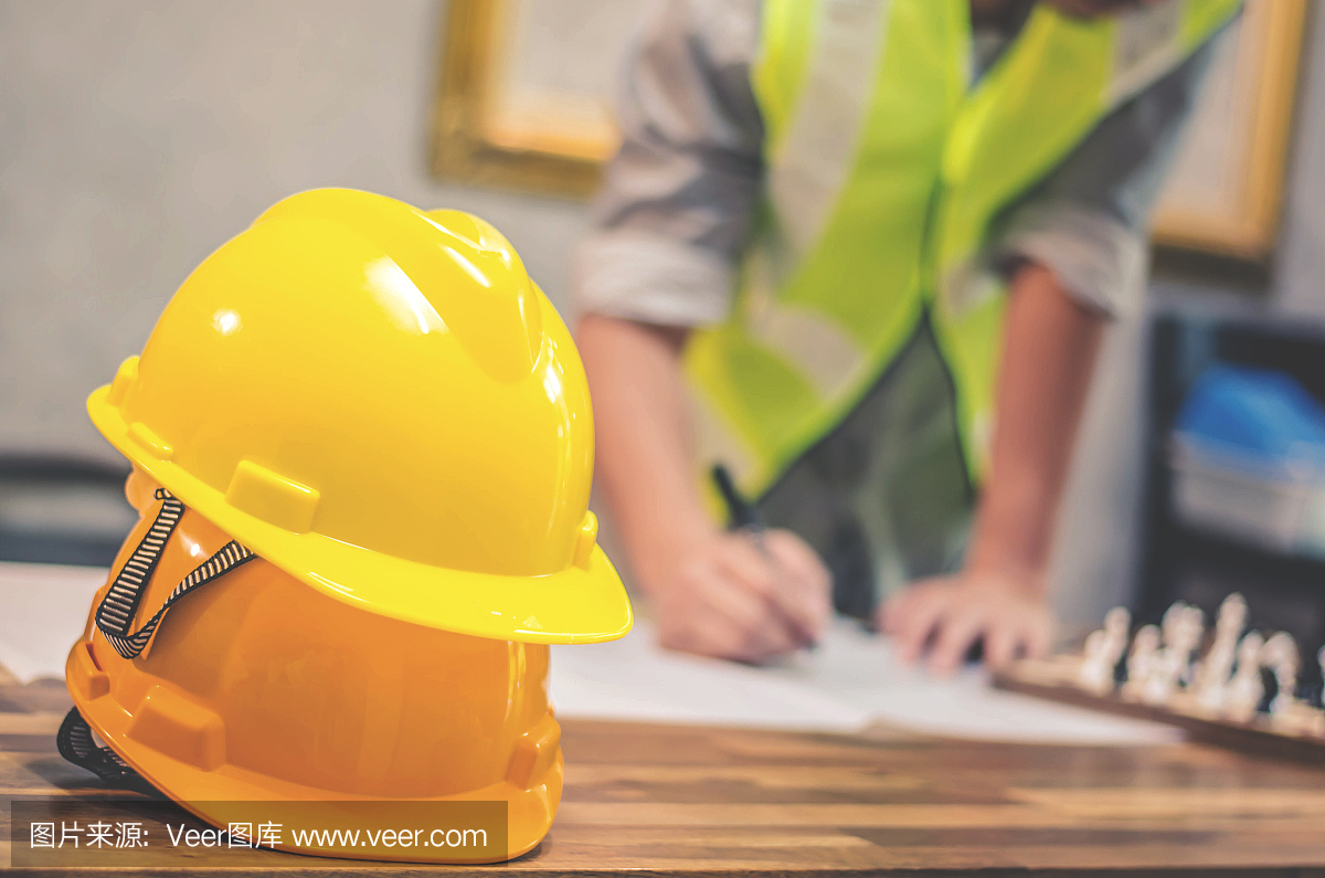 作为工程师或工人的工人安全工程用黄色硬质安全帽,施工现场桌上有工程施工项目蓝图
